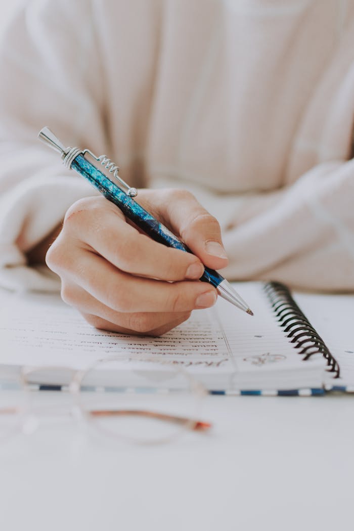 about-02 A detailed view of a hand writing notes with a pen in a spiral notebook.